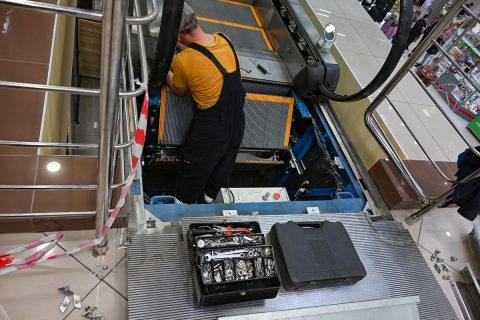 Man repairs escalator, steps inside, standing with her back near the step, tools are.